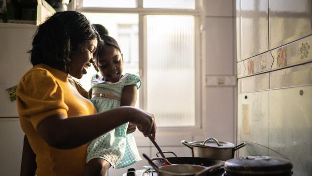 Women holding a child cooking on a stove