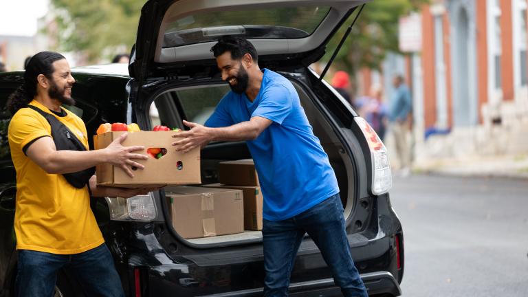Two people hand food to eachother outside a car