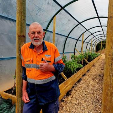 Man in orange shirt standing in front of a garden